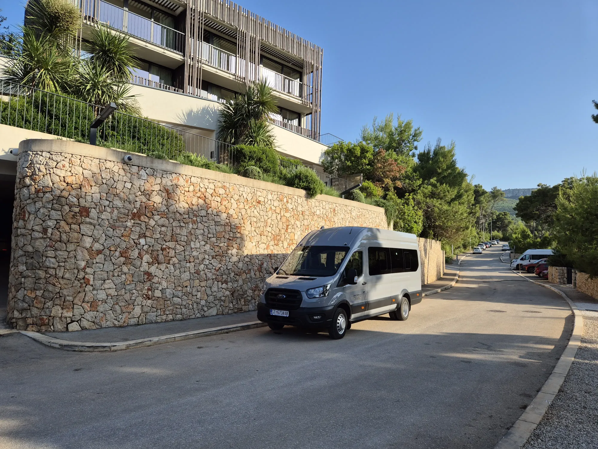 Silver group transfer minibus parked on a quiet road beside a stone-walled resort on Hvar