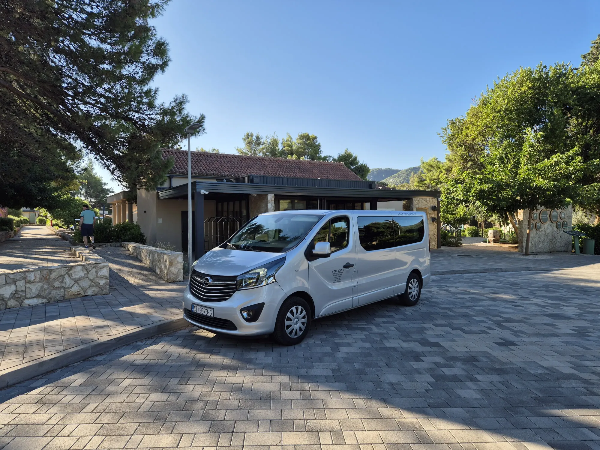 Silver passenger van for Hvar transfers parked on a paved drive in front of a stone resort building
